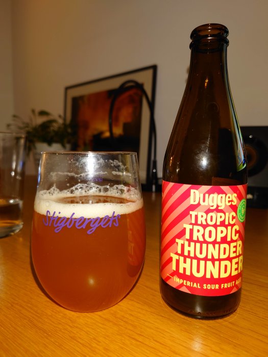 Ett glas med skummande öl och en tom ölflaska med etiketten "Dugges Tropic Thunder" på ett bord.