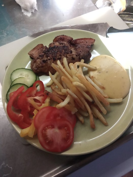 Tallrik med fläskstek, pommes frites, skivad tomat och gurka samt bearnaisesås.