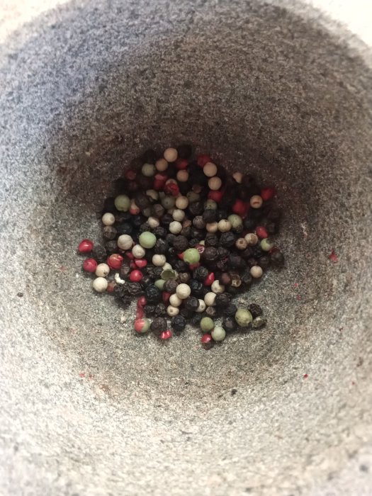 Blandade hela gröna, svarta och rosépepparkorn i en mortel.