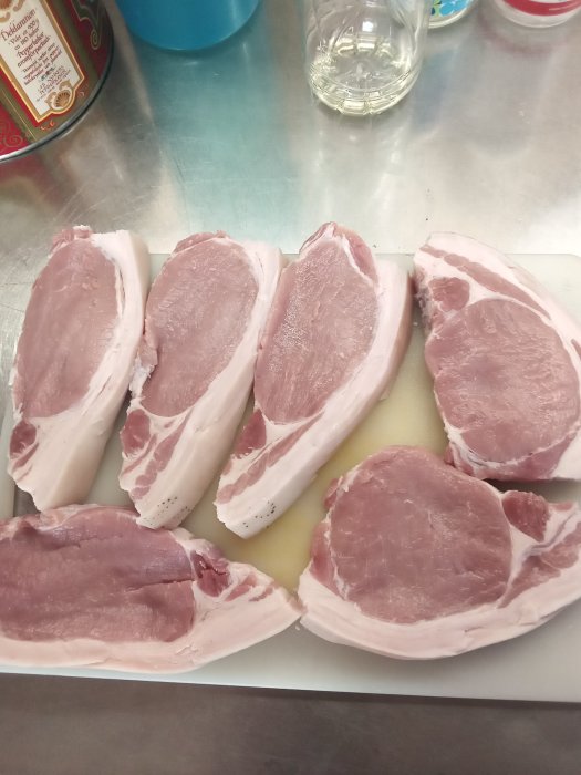 Sex stycken råa fläsksteksskivor med kappa på skärbräda, kryddade och redo för tillagning.