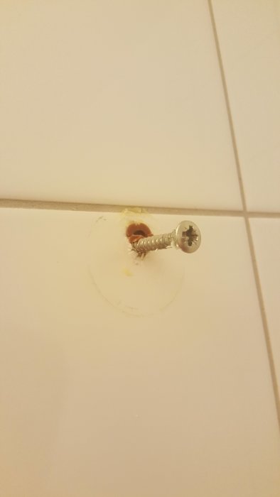 Skruv felsatt i väggkakel med synligt hål och skada runt, i ett nyligen tillträtt badrum.