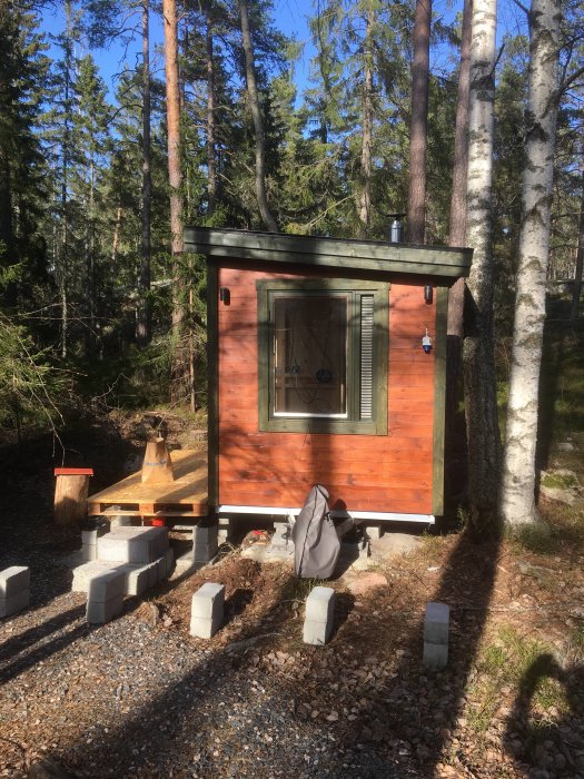 Trädgårdsbyggnad med elintag och belysning, löstagbar veranda under konstruktion, omgiven av skog.