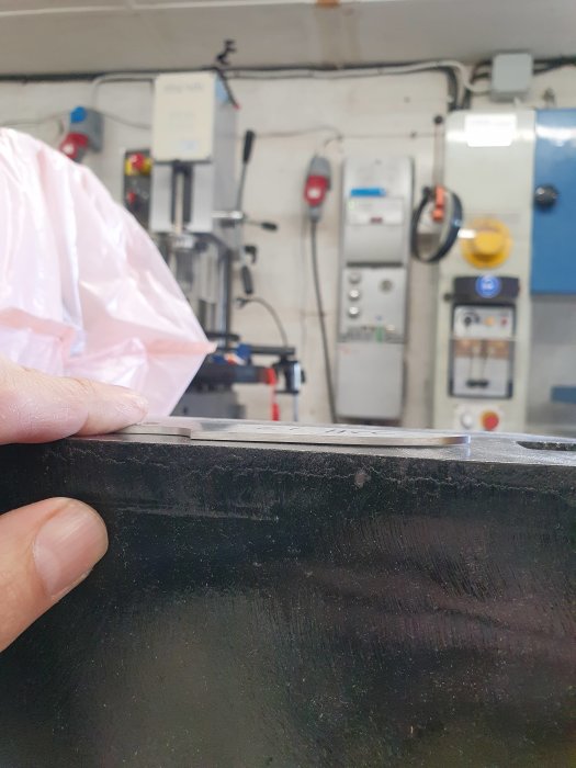 Hand som håller stålbit med böjning framför industrimiljö, illustrerar vrigningsproblem vid värmebehandling.