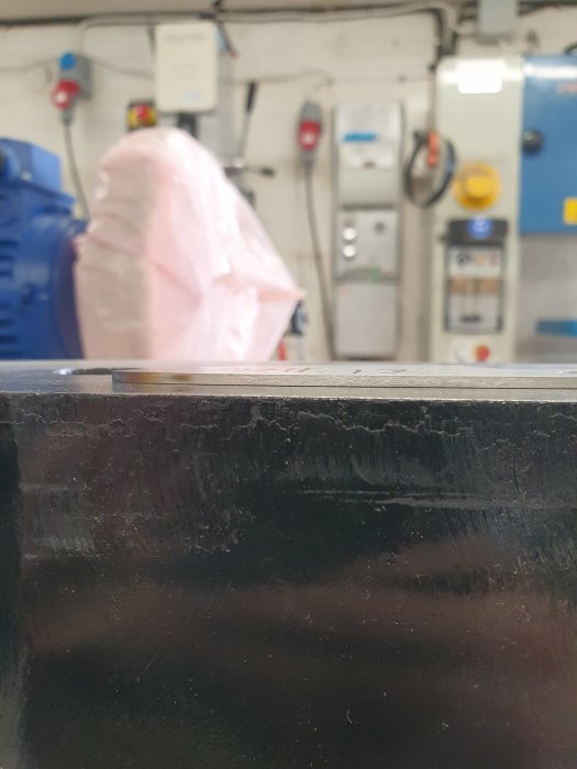 Närbild på en vriden stålplåt framför industrimaskiner i suddig bakgrund.