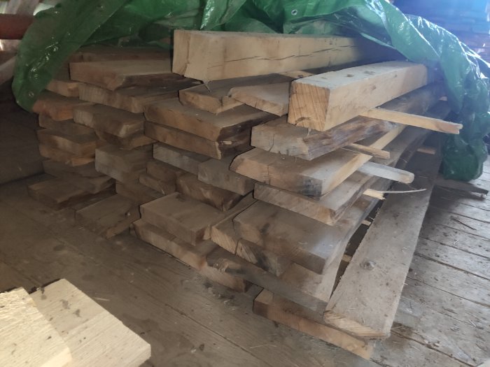 Stapel av grova ekplank i varierad längd och bredd för byggprojekt, lagrade inomhus.