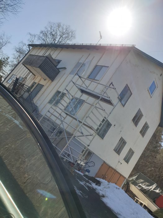 Byggnadsställning uppställd vid gaveln på ett vitt hus med reglar synliga och snö på marken.