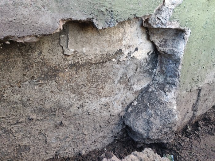 Stor spricka i en betongkonstruktion med synlig undermåligt armerad gjuten klack och matjord, vilket indikerar sättningsskador.