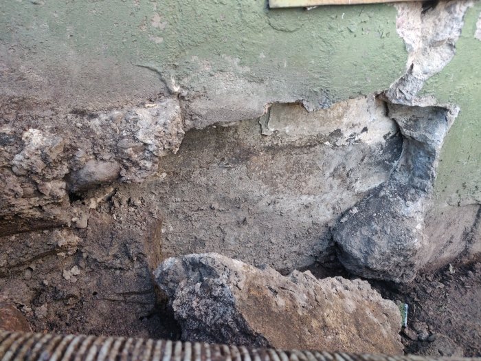 Spricka vid fasaden där ett undermåligt armerat och gjutet lager av betong vilar på matjord.
