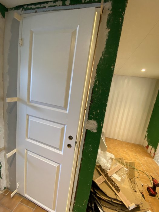 Vit dörr lutad mot väggen i ett rum under renovering med byggmaterial på golvet.