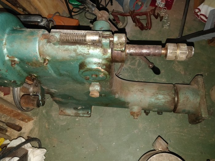 En grön gammal mekanisk enhet, möjligtvis en svarv eller pump, på ett verkstadsgolv.