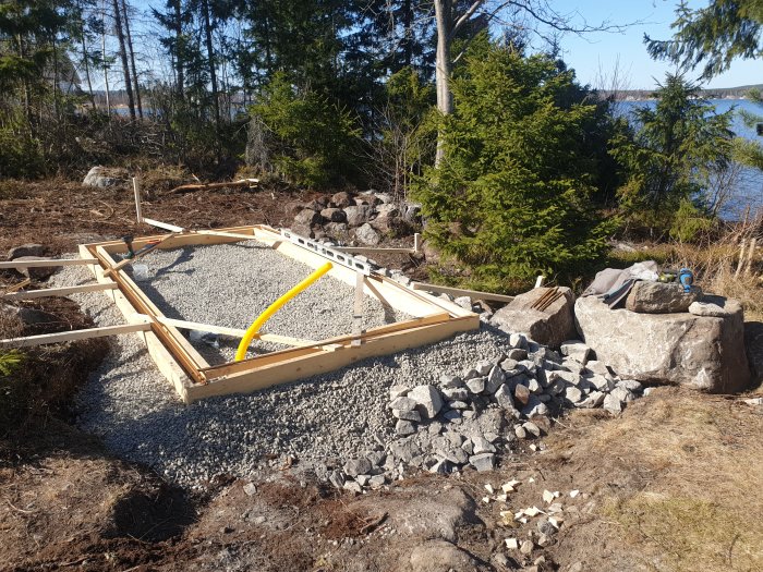 Form för gjutning och armeringsjärn vid ett byggprojekt för växthus med skog och sjö i bakgrunden.