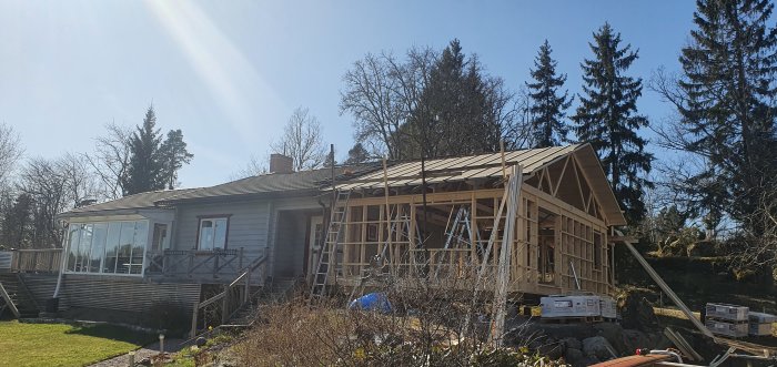 Ett pågående takbygge på ett hus med trästomme och ny pålagd takpapp, med byggmaterial synligt i förgrunden.