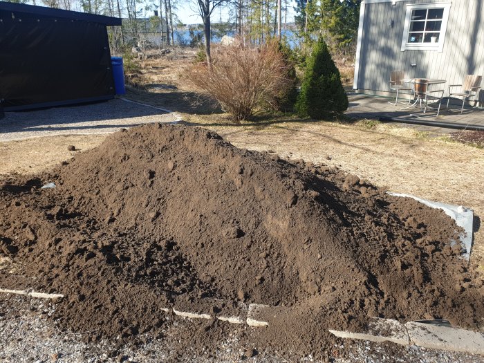 En hög med mörk matjord levererad på en grusuppfart bredvid en gräsmatta.