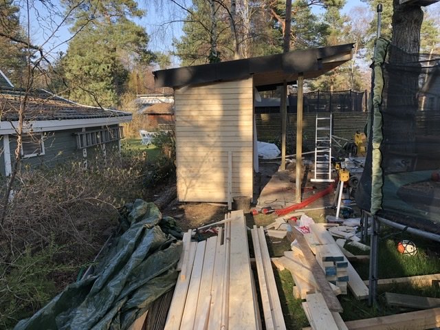 Byggplats med en pågående installation av fjällpanel på en byggnad bland trä- och isoleringsmaterial.