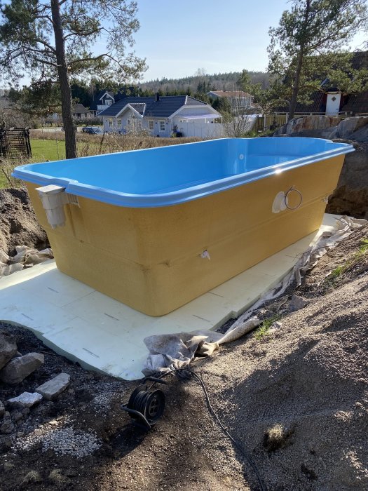 Nyinstallerad ovanmarkspool på förberedd mark med hus och träd i bakgrunden.