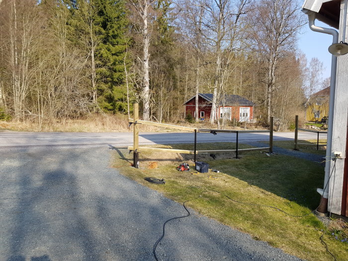 En pågående installation av staketreglar utmed en grusgång, med verktyg på marken och natur i bakgrunden.