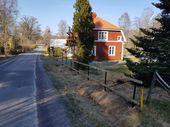 Nyinstallerade staketreglar längs en väg bredvid ett rött hus, stolparna ser i våg ut även om perspektivet kan bedra.