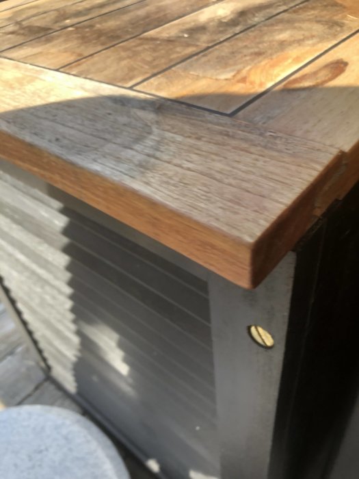Teakbox med fuktfläck på locket och sprucken kant i solljus.