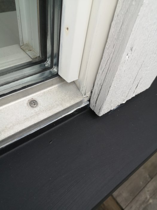 Närbild på ett fönsterbleck i metall vid träfönster, fäst med synliga skruvar, behöver underhåll.