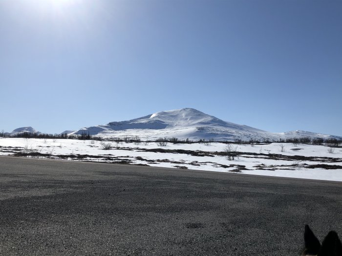Snötäckt bergslandskap med klarblå himmel och delvis isig väg i förgrunden.