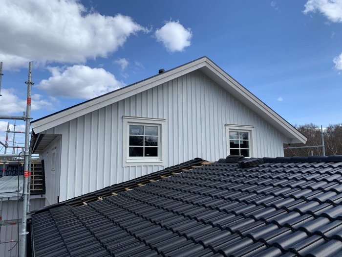 Nypanelat hus med svart tak, synliga takfönster och byggställningar under en klar himmel.