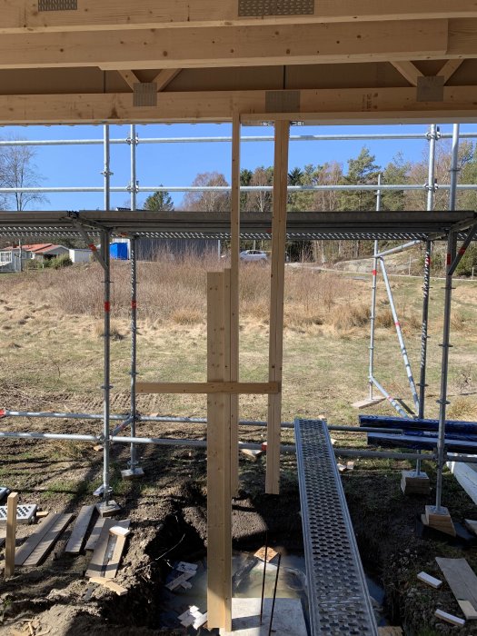 Nybyggd träkonstruktion för carport med stolpar, balkar och takstöd med byggmaterial och ställning i bakgrunden.