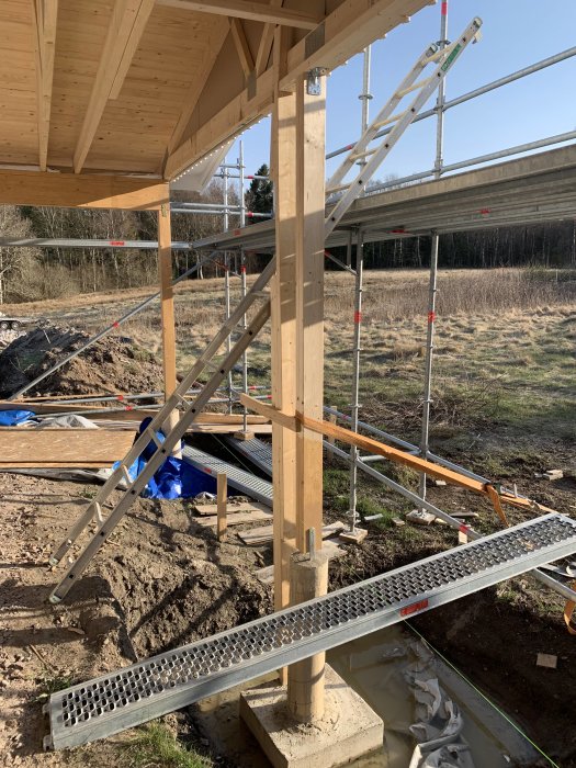 Konstruktion av carport med trästolpar och gjuten plint, med läkt och panel runt porten.