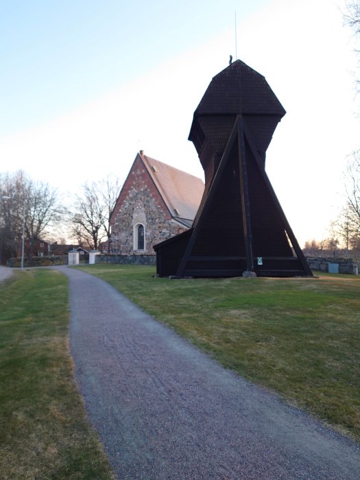 Stig framför en kyrka med klockstapel i trä och stenkyrka i bakgrunden under skymning.