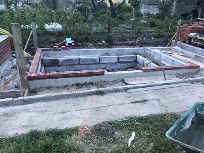 Grundläggning med lecablock för växthus under konstruktion, med synlig stenkross och byggmaterial.