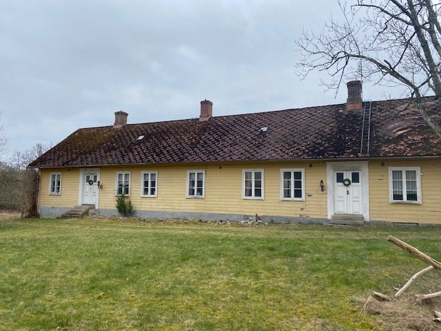 Gult äldre långt hus med tegeltak från tidig 1900-tal, möjligtvis med historiska detaljer.