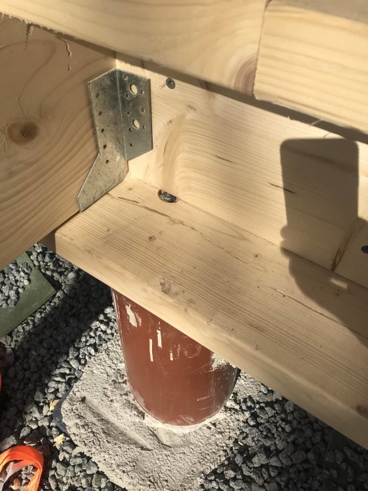 Trästomme förankrat med metallvinkel i plint, det syns virke och skruvar.