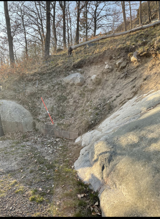 Brant slänt med sand, jord och stora stenar mellan bergknallar, erosionsskador synliga.