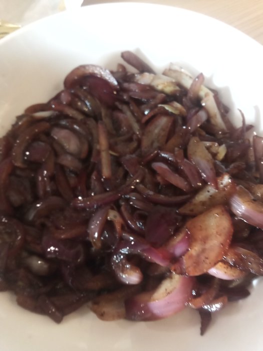 Stekt rimmat fläsk och rödlök i en vit tallrik, basen till en hemmagjord sås.