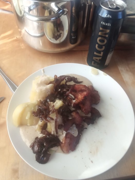 Tallrik med stekt fläsk, sås, rödlök och kokt potatis serverad med en burk folköl.