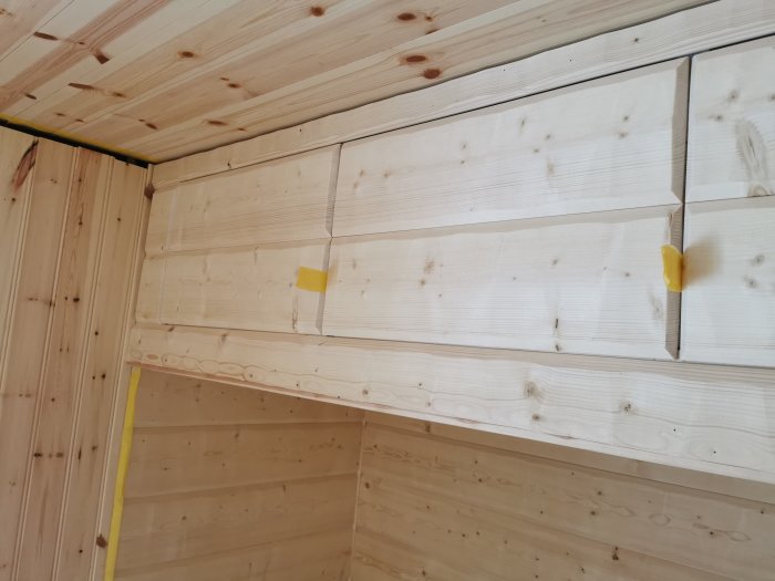 Hemmagjorda skåpluckor av bilade timmerpaneler på IKEA-stommar, med tejpmarkerade gångjärn.