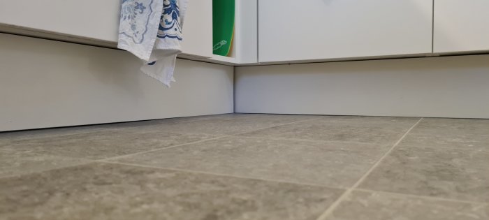 Vy under köksbänkar som visar golv och utrymmet där en LED-list kan installeras, med en hängande kökshandduk till vänster.