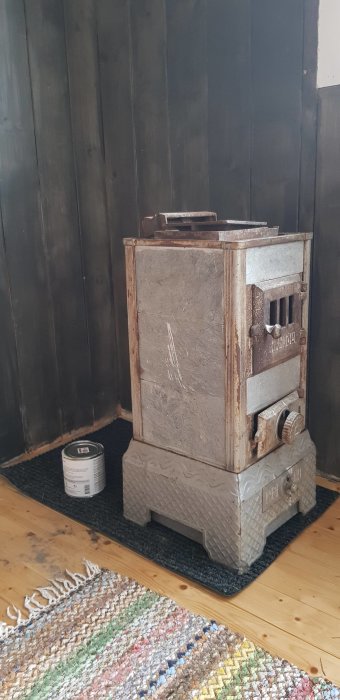 Gammal vedkamin av gjutjärn på svart matta med svarta träväggar och färgburk bredvid.