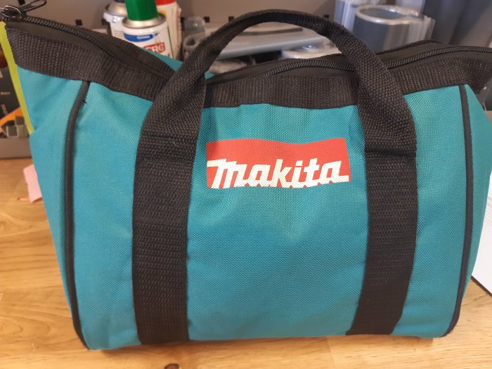 Turkos och svart väska med Makita-logotyp på en bänk, nämnd som en matdoseväska.