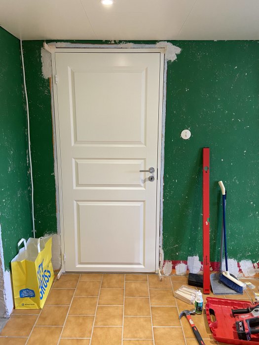 Nyinstallerad vit dörr i ett rum under renovering med gröna väggar och verktyg på golvet.