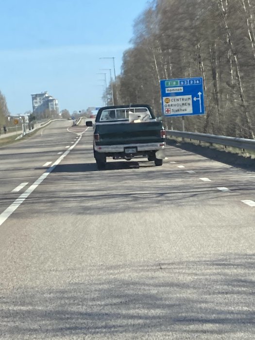 Pickup med flera lådor på flaket kör på motorväg, trafikskylt för E18 synlig.