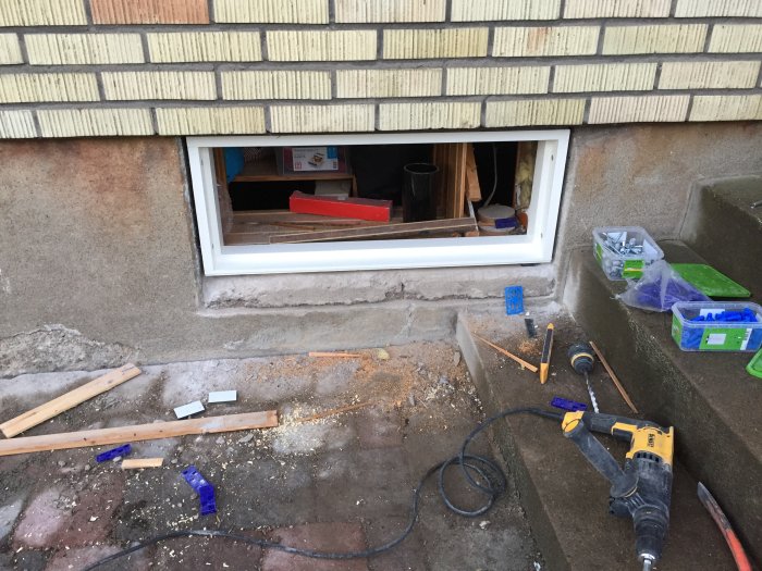 Ofärdigt fönster i vägg utan glas med verktyg och byggmaterial på marken.