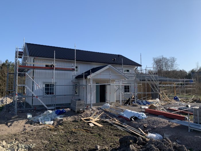 Nybyggt hus med byggnadsställningar, renkapad panel och installerade stuprännor.