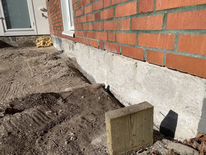 Hussockel med bortknackad puts vid tegelfasad, exponerande betongblock under renoveringsarbete.