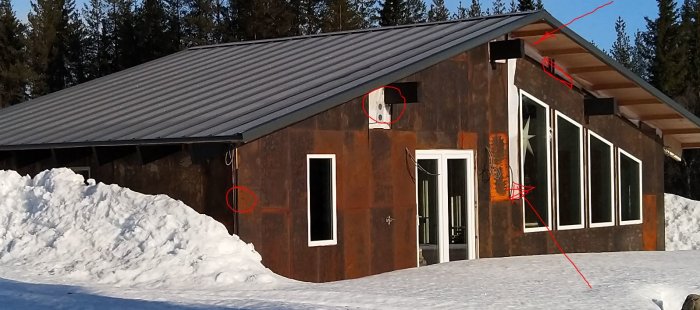 Ett hus med cortenstålklädd fasad och mörkt tak, omgivet av snö, med markeringar för kommande byggdetaljer.