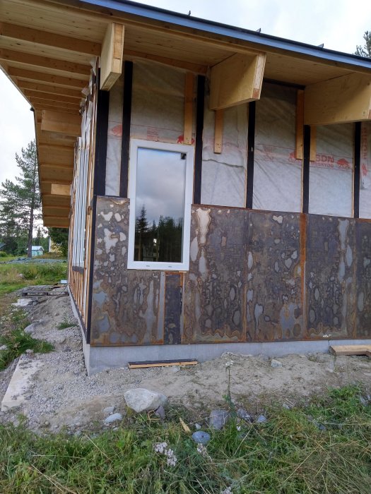 Hörn av ett hus under konstruktion med rostiga metallplattor och synliga träbalkar som fasadmaterial.