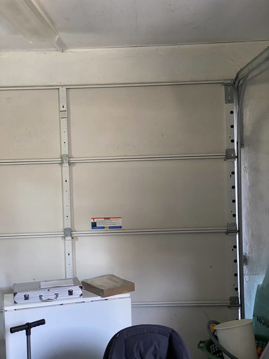 Oisolerad garageinteriör med felaktigt installerad port utan lister, handtag och lås.