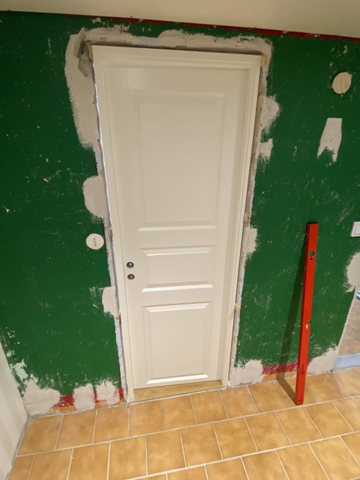 Nyinstallerad vit dörr i en vägg under renovering med synligt spackel och byggnivelleringsinstrument.