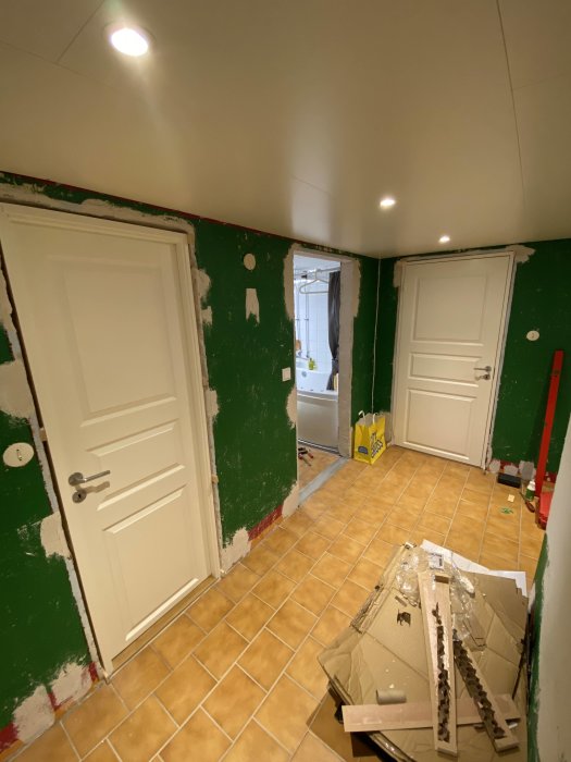 Renoveringsrum med gröna väggar, vita dörrar, gula klinkergolv och renoveringsmaterial på golvet.