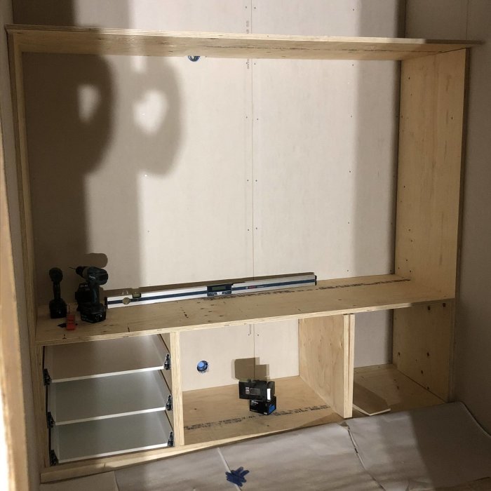 En outbyggd garderobsstomme av plywood med Ikea-lådor och verktyg inuti.