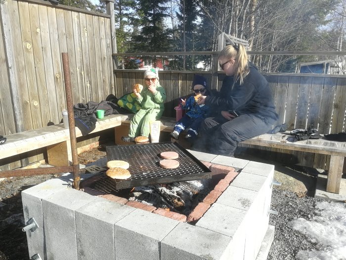 En familj avnjuter mat runt en hemmagjord murad grill av betongblock på en bakgård.